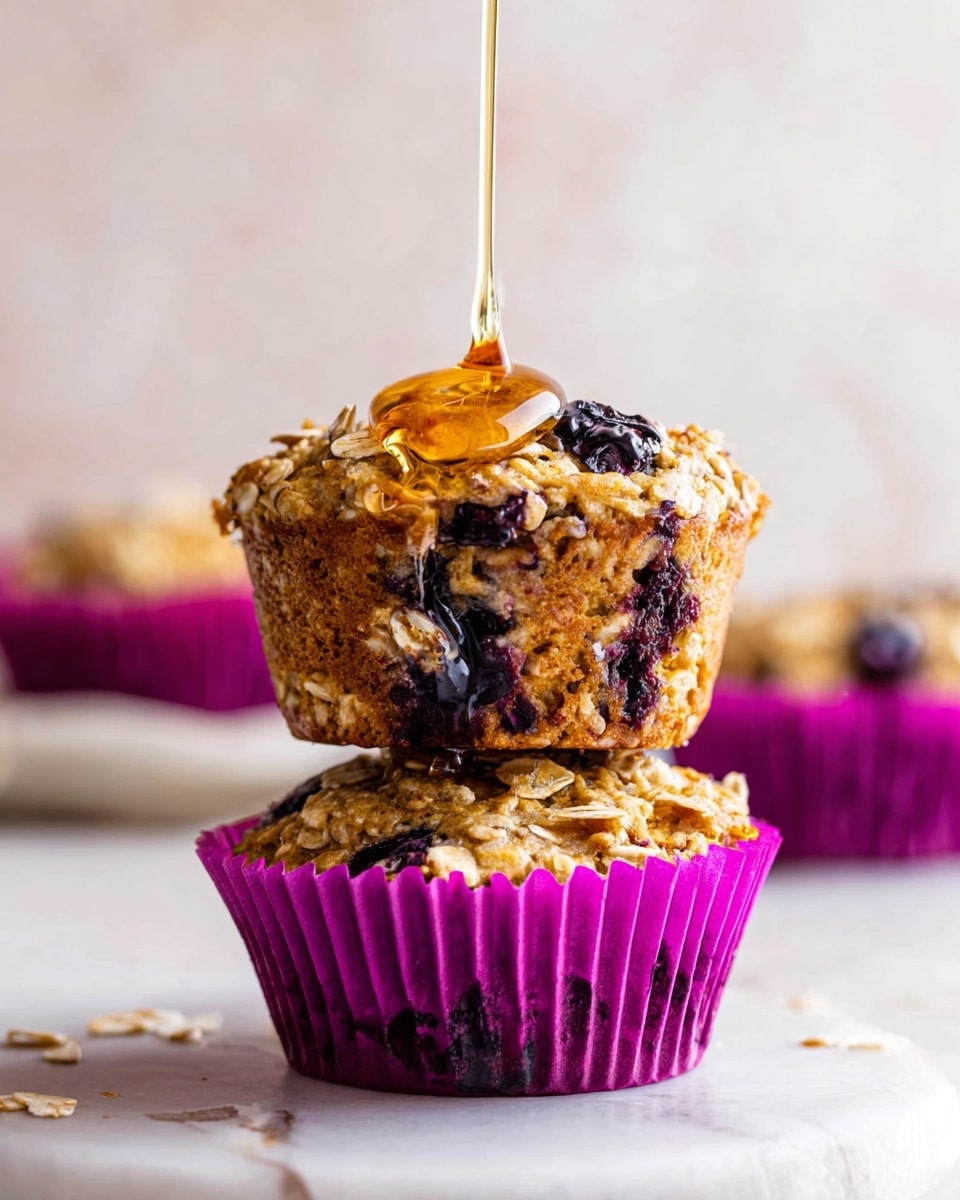 The image shows several blueberry muffins resting on a silver cooling rack placed on a white marbled surface. Each muffin is wrapped in a white and purple paper liner, with a rough textured top made of oats and whole blueberries scattered throughout. The muffins have a golden brown color, mixed with dark purple from the blueberries, and some oats sprinkled on top. Around the cooling rack, a few loose blueberries and droplets of honey or syrup add detail to the scene. The background is soft and out of focus, making the muffins the clear center of attention. photo taken with an iphone --ar 4:5 --v 7