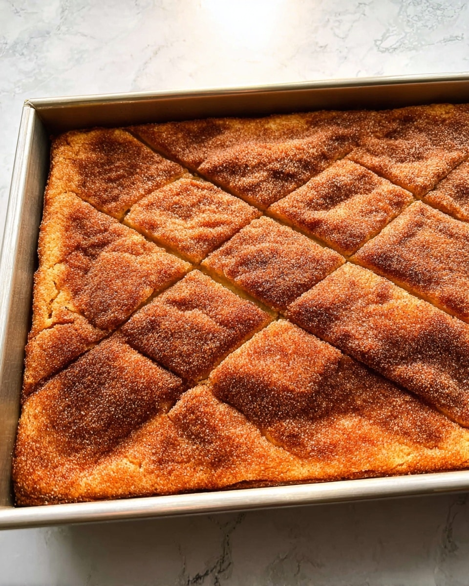A rectangular tray holds one thick layer of baked dessert with a firm, golden-brown surface covered in a cinnamon and sugar coating. The top layer has visible diagonal score lines creating large triangular sections across the dessert. The edges are slightly darker and crispier than the center. The tray rests on a white marbled surface photo taken with an iphone --ar 4:5 --v 7