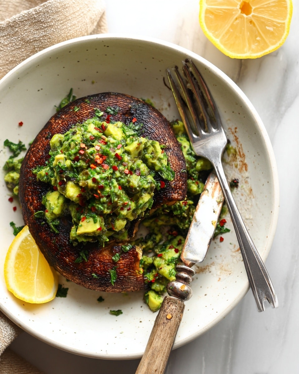 The image shows a white round plate with two thick, dark brown grilled patties that have a slightly charred texture on the surface. On top of the patties is a chunky green sauce made of chopped herbs and avocado pieces with a mix of vibrant green shades and tiny red chili flakes. A small wedge of lemon rests on the right side of the plate near the second patty. A silver vintage-style fork and knife are placed diagonally on the right side of the plate, with the knife resting partially on the food. The plate sits on a beige cloth over a white marbled surface. Photo taken with an iphone --ar 4:5 --v 7