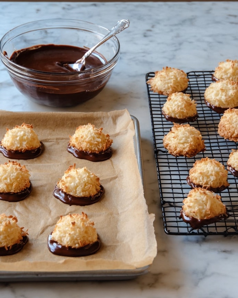 The image shows two groups of coconut cookies on a white marbled surface. On the left, nine cookies are on a baking sheet lined with brown parchment paper, each cookie partially dipped in dark brown melted chocolate at the base, forming a glossy and smooth layer that spreads out slightly under each cookie. The cookies themselves are light golden brown, round with a rough and crispy texture on top, sitting upright on their chocolate bases. Behind these cookies is a clear glass bowl filled with more shiny melted chocolate and a metal spoon resting inside. On the right, thirteen plain coconut cookies without chocolate are laid out on a black wire cooling rack. These cookies have a similar rough and golden toasted texture and are evenly spaced. The whole scene is lit softly, highlighting the textures and colors. Photo taken with an iphone --ar 4:5 --v 7