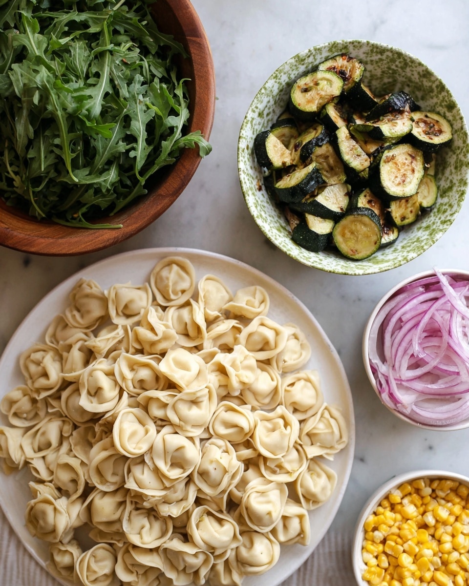 The image shows a white plate filled with a large pile of uncooked tortellini pasta, each piece light beige and tightly folded into small round shapes. Above it, a white bowl decorated with green speckles holds cooked zucchini pieces that are dark green with golden-brown edges. To the right, there are two smaller bowls, each white on the inside: one with bright yellow corn kernels and another with thin slices of raw red onion that are pale purple with a translucent texture. On the left side, a large wooden bowl contains fresh green arugula leaves that have jagged edges. All the dishes rest on a white marbled surface photo taken with an iphone --ar 4:5 --v 7
