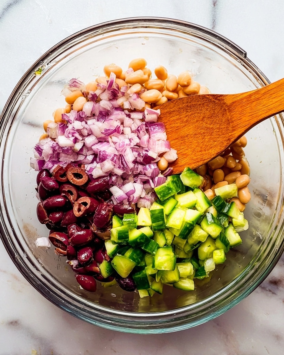 A clear glass bowl filled with four layers of ingredients, set on a white marbled background. The bottom layer consists of chopped purple onions with a slightly rough texture, spread evenly across one side. Next to the onions, there are sliced dark purple olives with a smooth, shiny surface. Above the onions and olives, small light beige beans form a scattered layer with a soft texture. Close to the beans, there are bright green cucumber pieces cut into small cubes with a fresh, moist look. On the right side, a wooden spoon with a warm brown color rests inside the bowl, partially covering the ingredients. Photo taken with an iphone --ar 4:5 --v 7