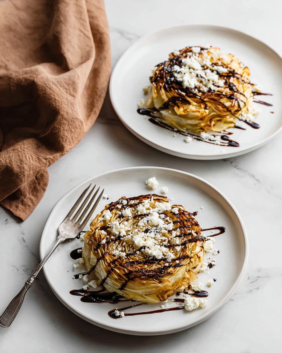 Two white plates sit on a white marbled surface, each holding a stack of thin, golden brown cabbage slices layered like a small round cake. On top of each cabbage stack is a drizzle of dark balsamic glaze creating thin, shiny lines, and scattered white crumbly cheese adding texture and contrast. One plate in the lower part of the image has a silver fork resting against its edge, while the upper plate is bare. A soft brown cloth is casually placed to the right side of the top plate, enhancing the cozy presentation light and shadows play gently on the food and surface, giving depth to the layers. Photo taken with an iphone --ar 4:5 --v 7