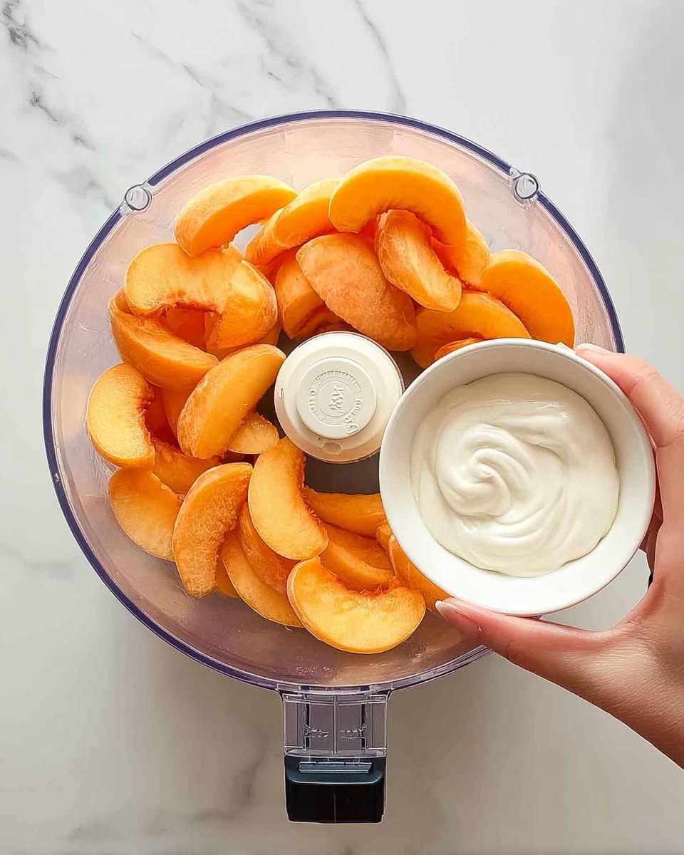 A clear food processor bowl is filled with bright orange peach slices, arranged in one layer around the center blade. A woman's hand is holding a small white bowl above the processor, pouring thick, smooth white cream into the peach slices. The scene is set on a white marbled surface. photo taken with an iphone --ar 4:5 --v 7