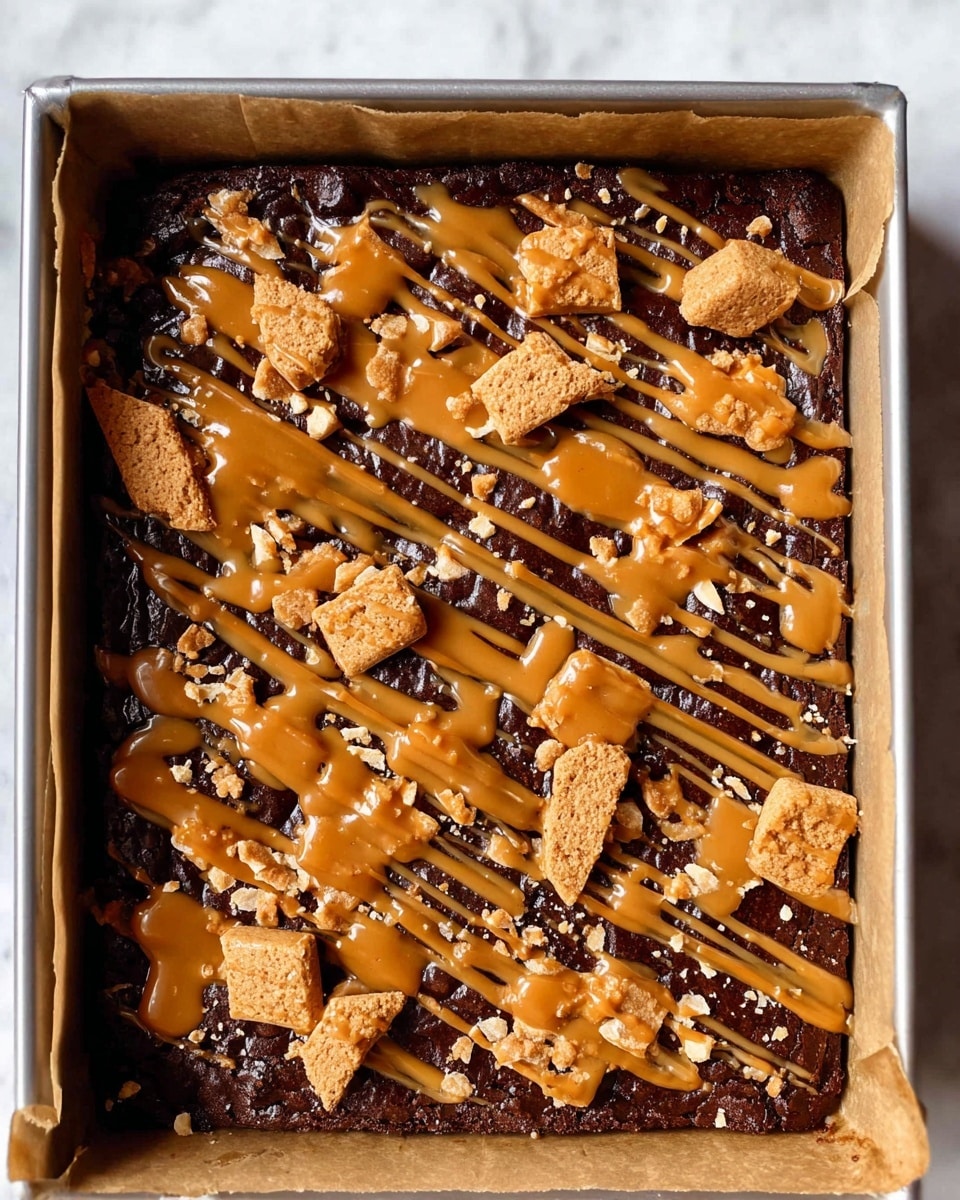 The image shows a baking tray lined with parchment paper, filled with one thick, dark brown brownie layer. On top of the brownie are whole and broken light brown cookie pieces scattered all over. A caramel-colored sauce is drizzled over the cookies in uneven thin stripes, adding a shiny texture. The tray sits on a white marbled surface. Photo taken with an iphone --ar 4:5 --v 7