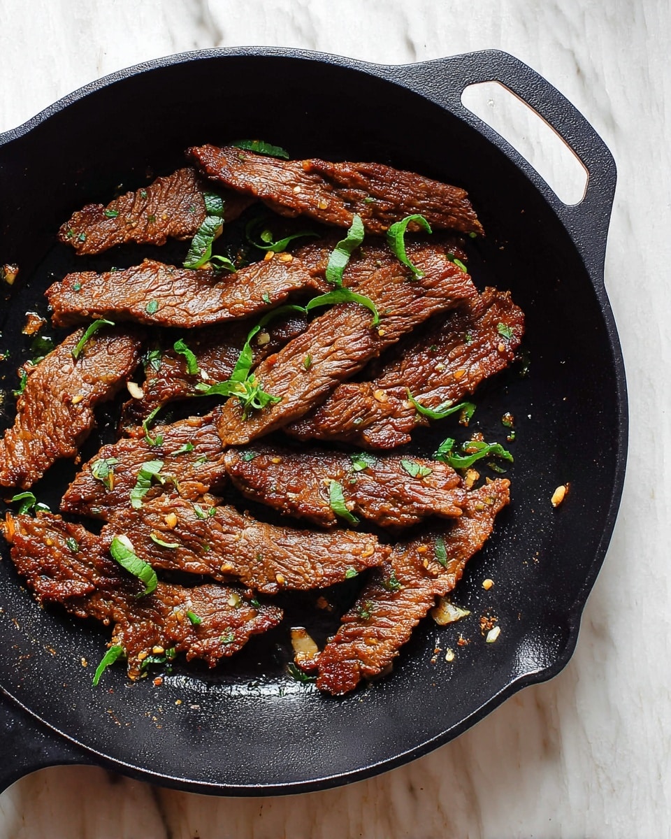 A black cast iron pan holds several pieces of cooked meat strips, arranged loosely across the pan’s surface. The meat is brown with a slightly textured, crispy look and is sprinkled with small fresh green herb leaves, adding pops of color. There are tiny bits of garlic or seasoning scattered around the meat. The pan rests on a white marbled surface. photo taken with an iphone --ar 4:5 --v 7