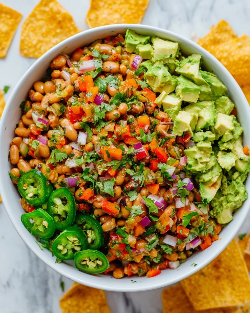 A white bowl filled with a colorful bean salad, showing three main layers: the base layer has light brown beans mixed with small diced red, orange, and green bell peppers, along with finely chopped purple onions; the middle layer has chunks of green avocado and sliced green jalapeños, adding texture and freshness; the top layer is sprinkled with chopped green cilantro and a few sliced jalapeños for garnish. The bowl is placed on a white marbled surface, with scattered yellow tortilla chips around it. Photo taken with an iphone --ar 4:5 --v 7