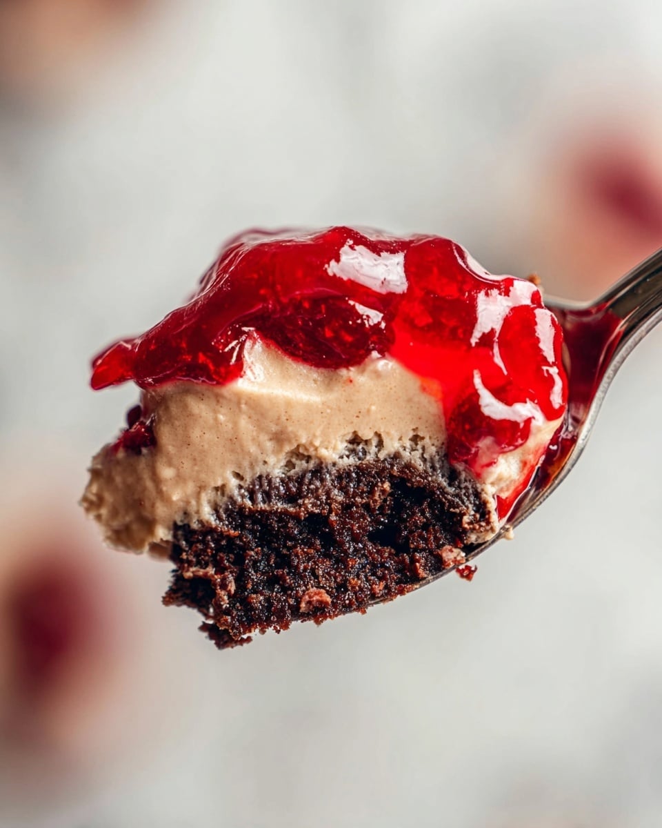 A close-up of a spoonful of dessert with three layers: the bottom layer is dark and crumbly like chocolate cake, the middle layer is smooth and creamy with a light brown color, and the top layer is a glossy bright red jelly. The spoon is silver and the background shows a soft white marbled texture. The photo is focused on the dessert, showing creamy and glossy textures clearly photo taken with an iphone --ar 4:5 --v 7
