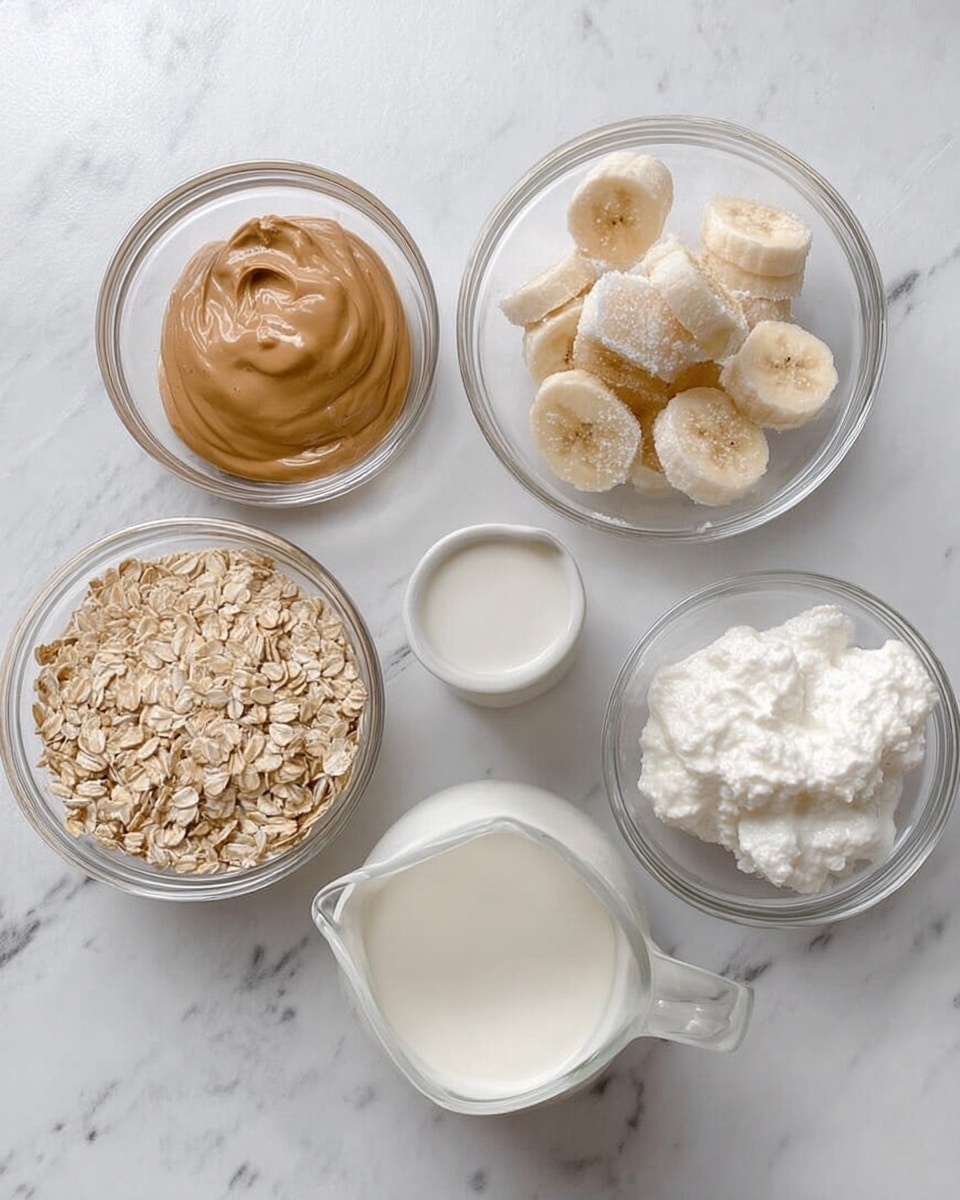 The image shows five clear glass bowls and a small white pitcher arranged on a white marbled surface. The top left bowl contains a smooth light brown cream with a glossy texture. Next to it on the right, a bowl holds frozen banana slices covered lightly with ice crystals. To the right of that is a bowl with a white, soft, and fluffy creamy substance. Below those, on the bottom left, a small bowl has plain rolled oats with a light tan color and rough texture. Beside it, a white pitcher is filled with a smooth, creamy white liquid. photo taken with an iphone --ar 4:5 --v 7