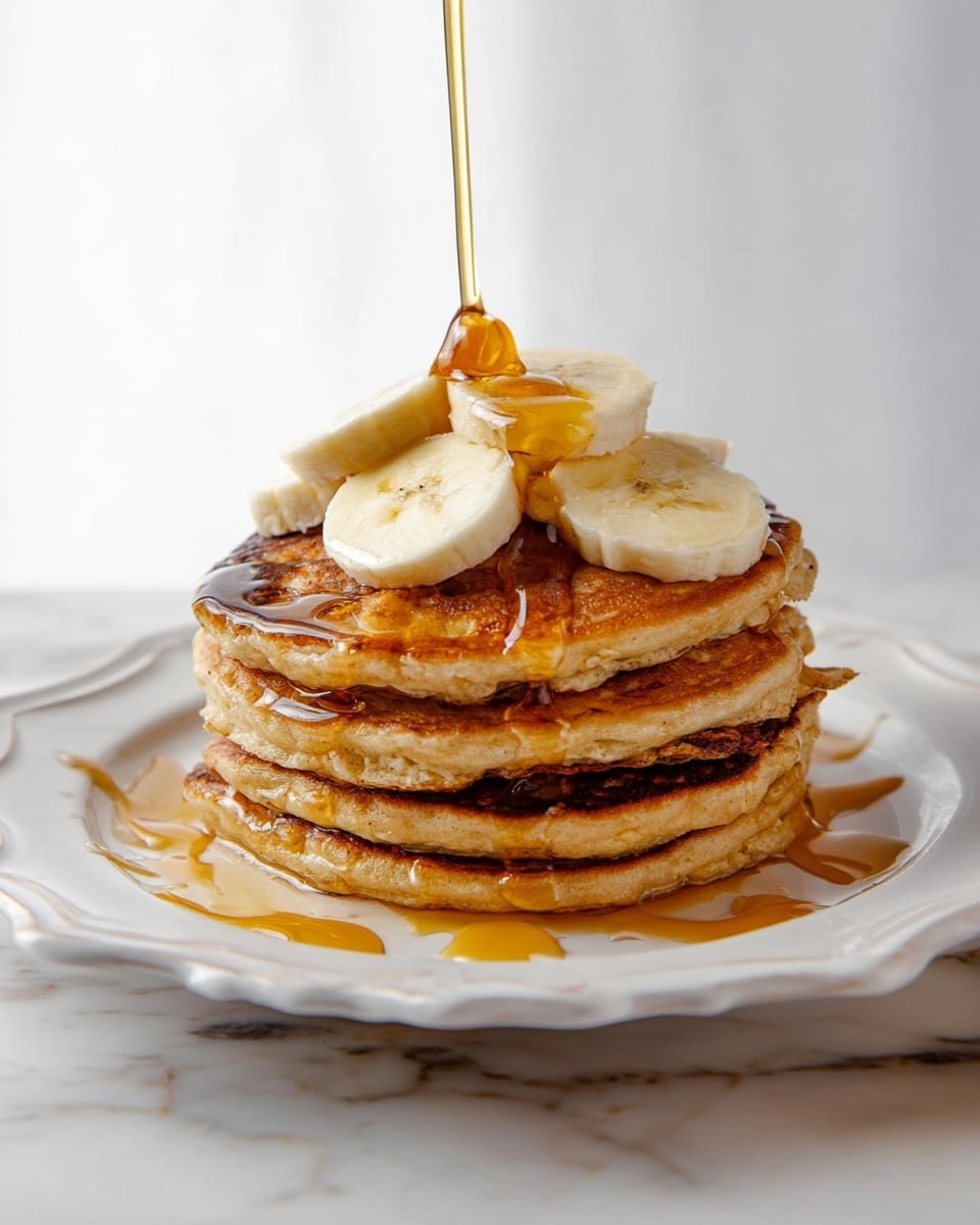 A stack of four golden-brown pancakes sits on a white plate with scalloped edges, each pancake showing a slightly different texture from fluffy to a bit crisp. On top of the stack are five thick banana slices arranged loosely, with some syrup pooling around them and beginning to drip down the sides. A stream of syrup is being poured from above, catching the light as it flows, adding a shiny golden layer over the soft and warm pancakes. The plate rests on a surface with a white marbled texture, creating a clean and bright background. photo taken with an iphone --ar 4:5 --v 7