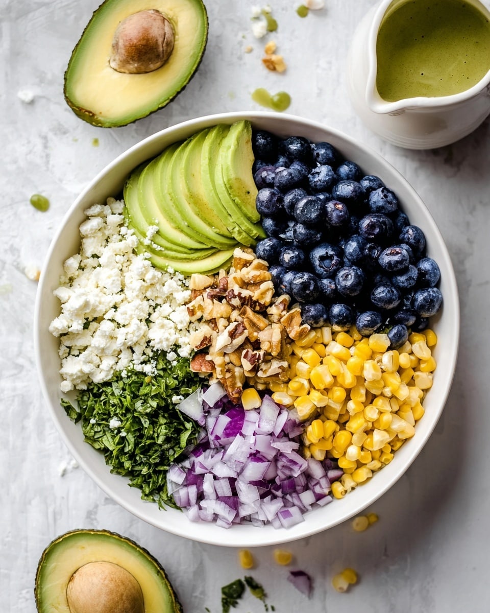 A white bowl filled with seven layers of food arranged side by side in a circular pattern, starting at top left with pale green avocado slices, followed by a layer of white crumbly cheese, then dark blue blueberries filling the top right quarter. In the center is a layer of light brown chopped nuts, moving down to yellow corn kernels at the bottom right. Next to the corn is chopped light purple onion, then green chopped herbs, and finally more pale green avocado slices at the bottom left. The bowl is placed on a white marbled surface with a halved avocado and a small white pitcher with green dressing nearby. Photo taken with an iphone --ar 4:5 --v 7