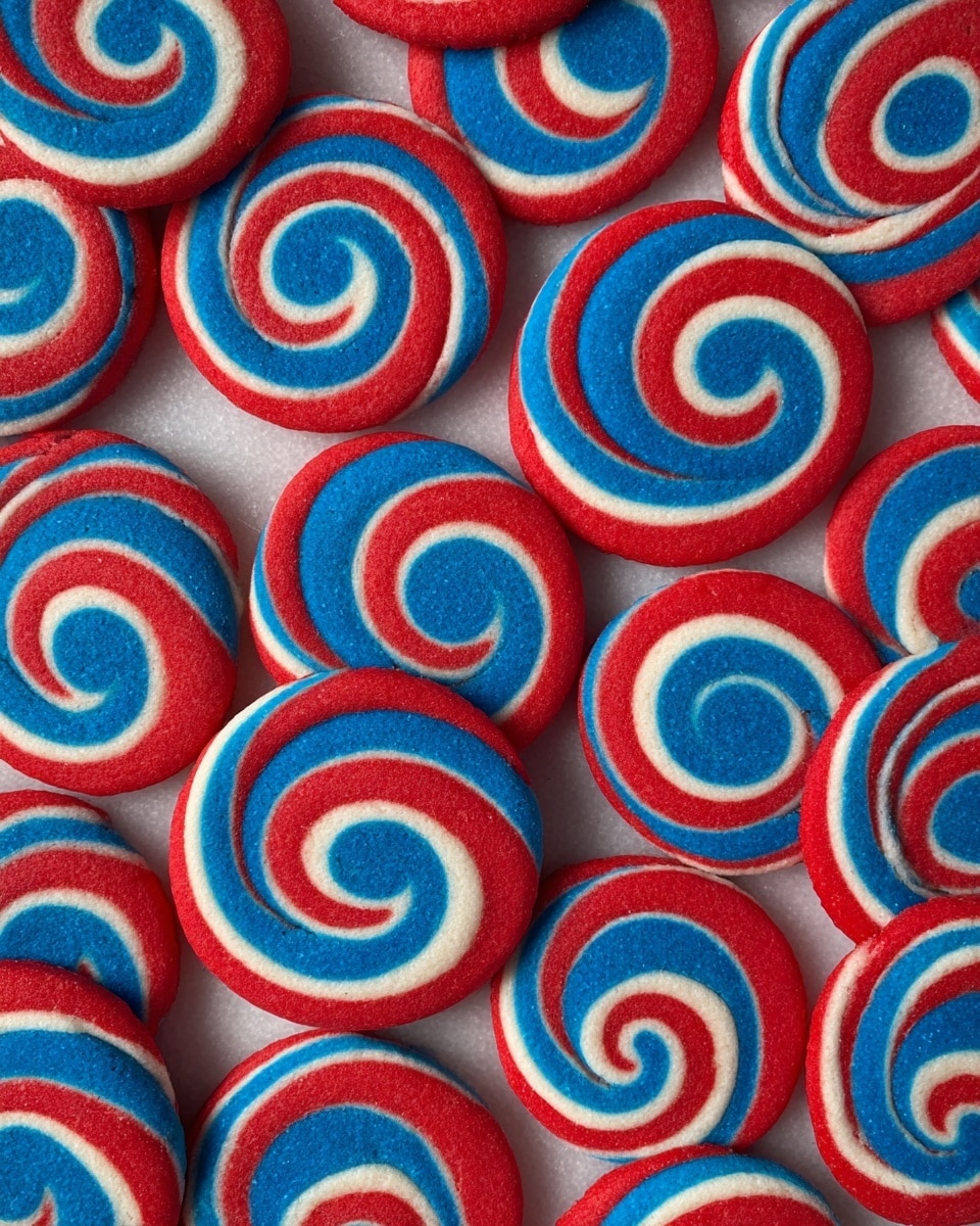 The image shows many round spiral cookies arranged in a tight grid on a white marbled surface. Each cookie has three colored layers twisted evenly in a swirl pattern starting from the center: a bright red outer ring, a white middle ring, and a vivid blue innermost ring. The cookies have smooth edges and a slightly textured surface that shows their baked dough. The repeated spiral design creates a vibrant red, white, and blue pattern across the whole image. photo taken with an iphone --ar 4:5 --v 7