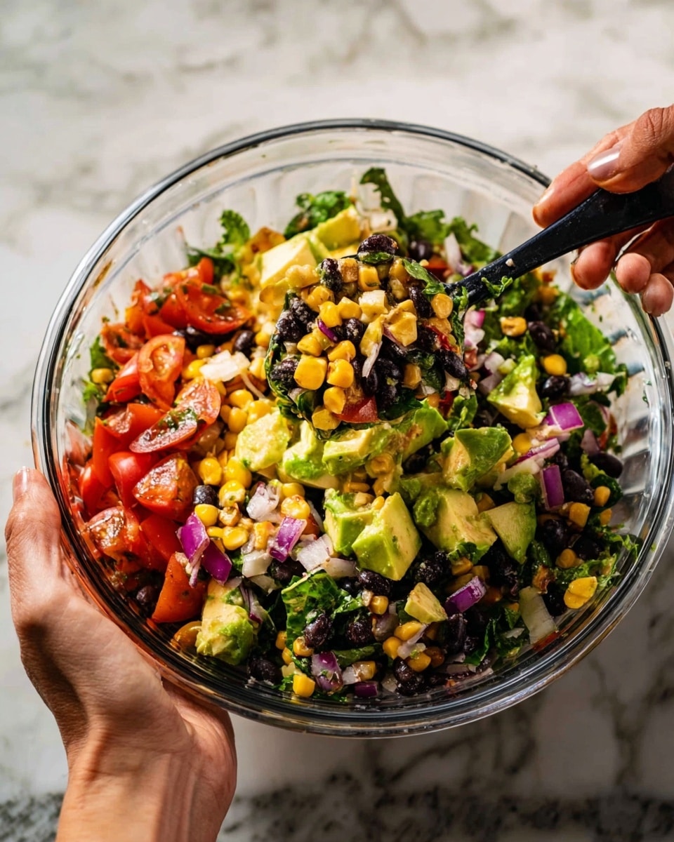 A clear glass bowl filled with a colorful mixed salad held by two woman's hands, one on each side of the bowl. The salad has layers of black beans, bright yellow corn kernels, green avocado chunks, red tomato pieces, purple onion slices, and fresh green leafy herbs. The mix is being stirred with a black spoon, lifting a portion that shows the varied textures and colors all mixed together. The background is a white marbled surface. photo taken with an iphone --ar 4:5 --v 7