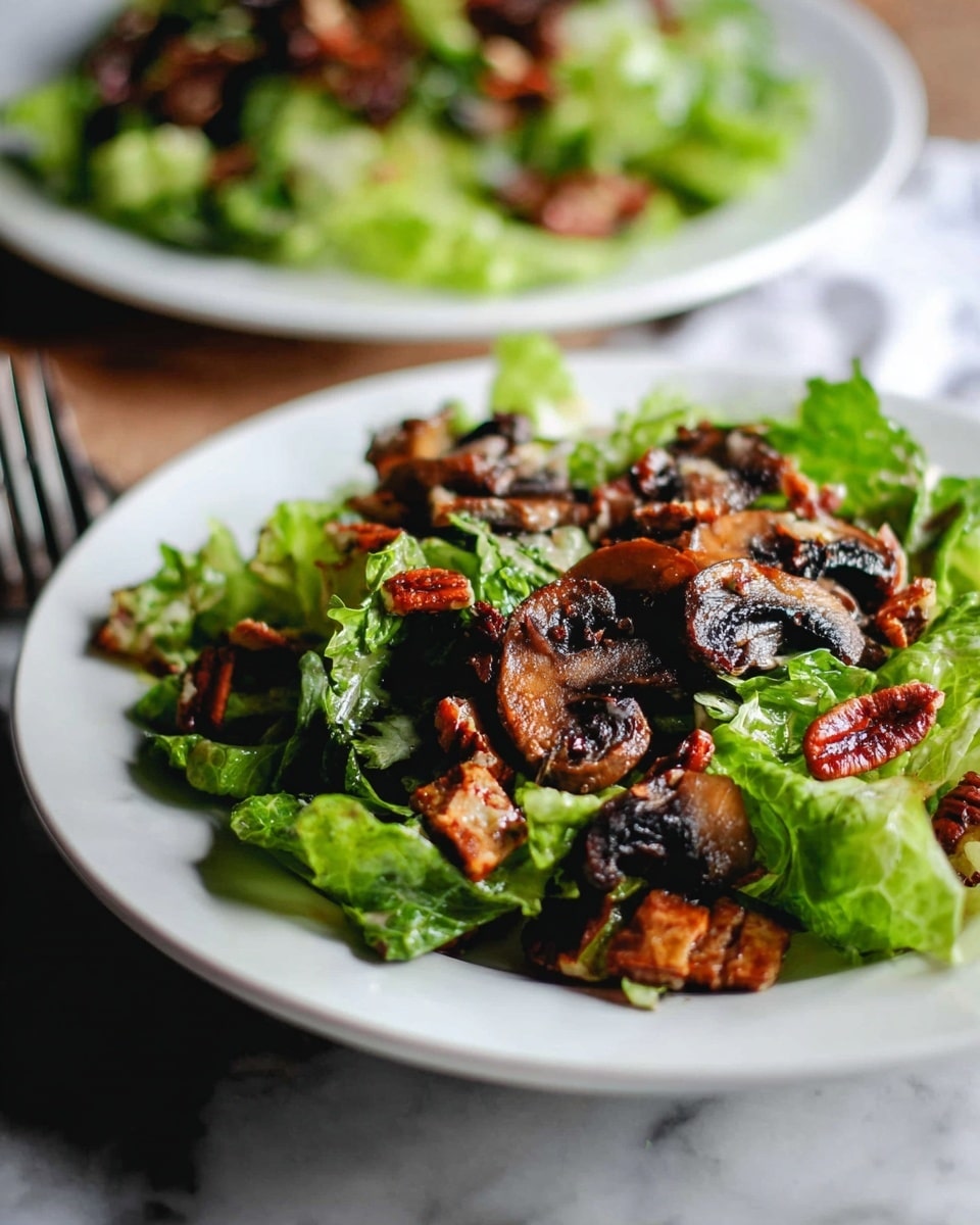 A white plate holds a fresh salad layered with bright green leafy lettuce as the base, topped with dark brown, grilled mushrooms that show a slightly charred texture. Scattered among the mushrooms are pieces of reddish-brown pecans, adding a crunchy element. The plate sits on a white marbled surface with part of another similar salad plate blurred in the background, creating depth. The lighting highlights the varying textures and colors, making the dish look fresh and appetizing photo taken with an iphone --ar 4:5 --v 7