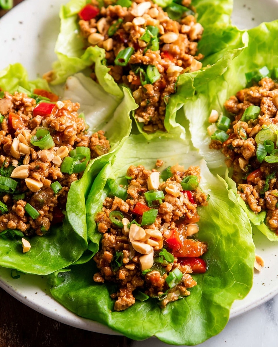 This image shows four lettuce wraps arranged on a white plate placed on a white marbled surface. Each wrap has a bright green, crisp lettuce cup as the base, topped with a mixture of finely chopped cooked meat, red bell peppers, and onions in a brown sauce. The meat mixture has a moist texture and is sprinkled with chopped green onions and chopped peanuts, adding a crunchy look on top. The wraps are close together, showcasing fresh and colorful layers of ingredients. photo taken with an iphone --ar 4:5 --v 7