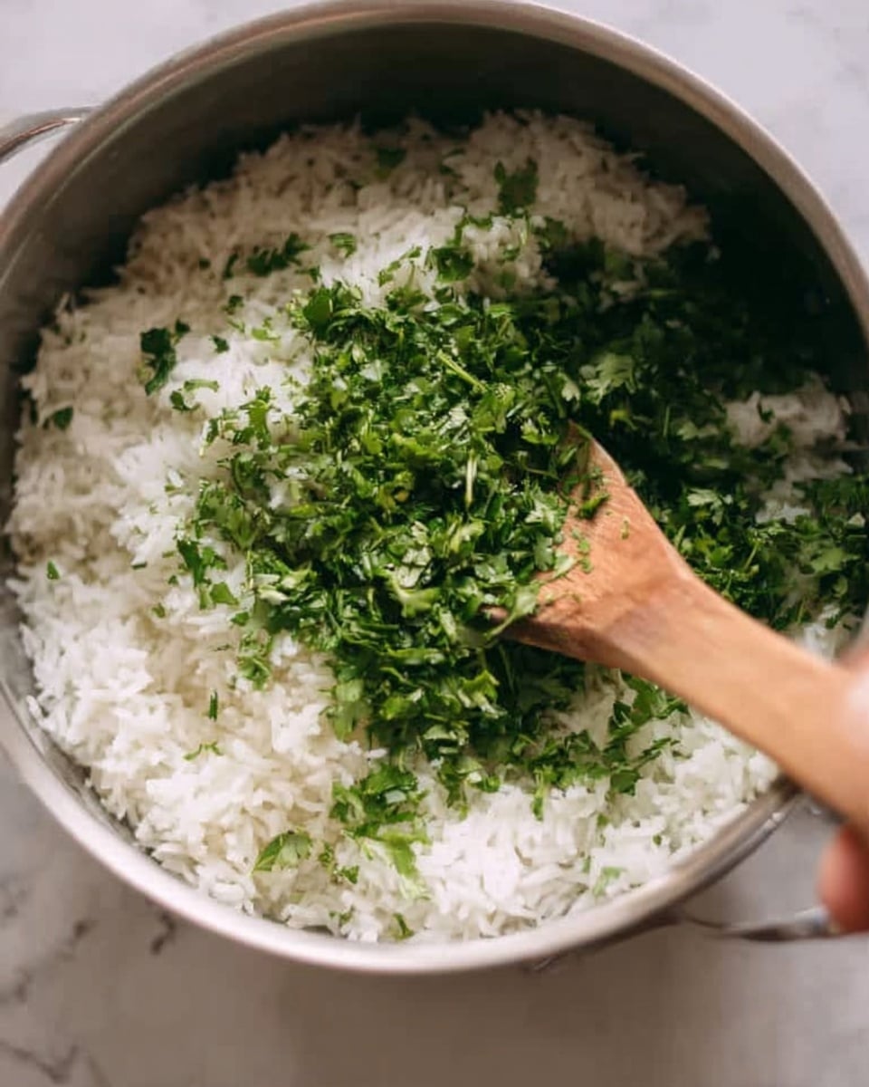 A close-up image of a pot filled with white cooked rice, topped with a generous amount of chopped fresh green herbs. A wooden spoon held by a woman's hand is mixing the herbs and rice together. The background shows a white marbled texture. photo taken with an iphone --ar 4:5 --v 7