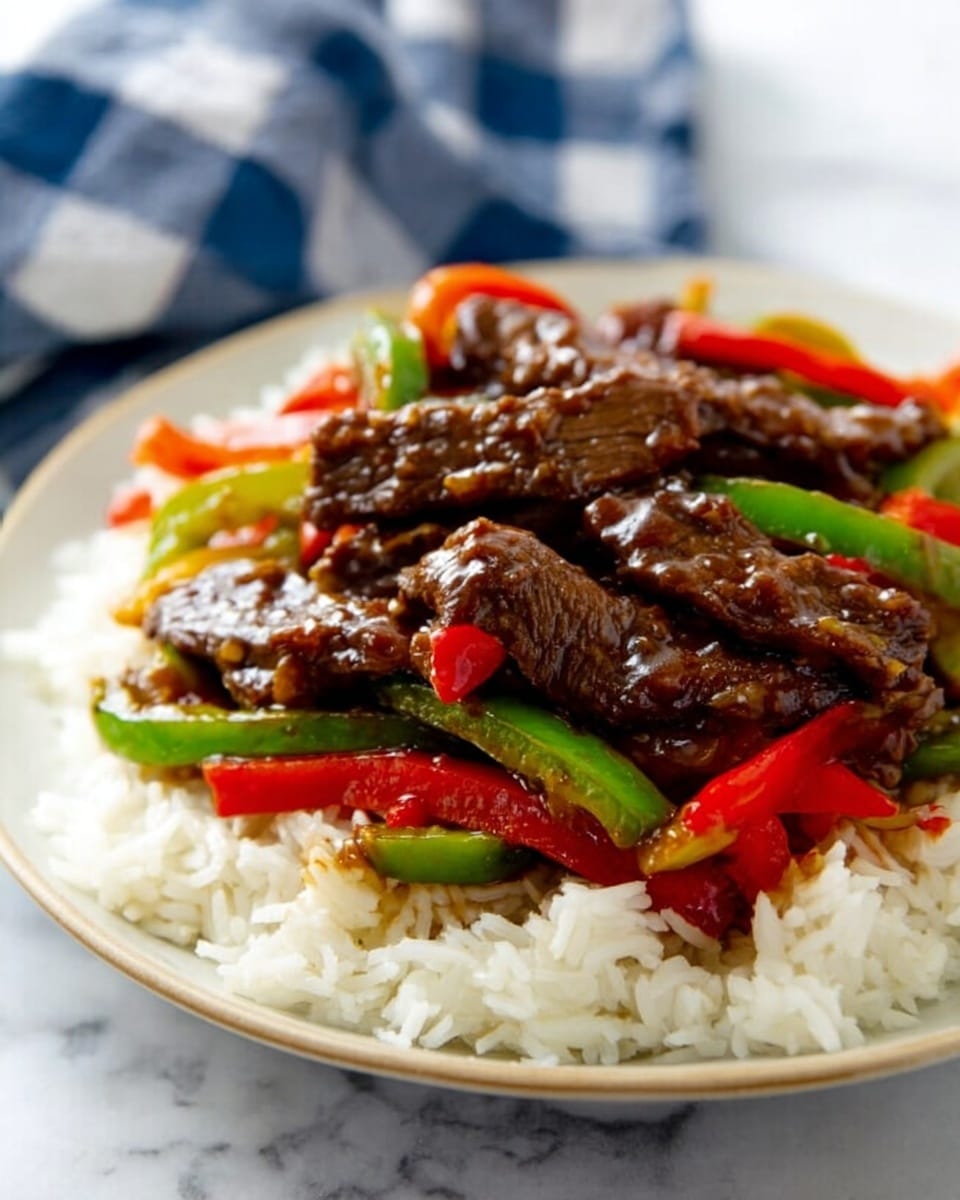 A white plate with a bed of white rice as the bottom layer, topped with a colorful mix of green and red bell pepper strips evenly spread over the rice. Over the peppers and rice, there are several pieces of dark brown, saucy beef strips stacked in the center, coated with a shiny, thick sauce. The plate sits on a white marbled surface, and a blurred blue and white checkered cloth is visible in the background. photo taken with an iphone --ar 4:5 --v 7