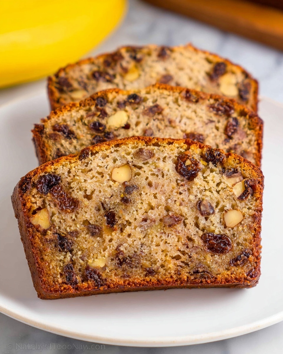 The image shows three slices of banana nut bread placed side by side on a white plate. Each slice has a golden brown crust with a moist, speckled light brown inside, filled with dark brown raisins and light tan nut pieces spread evenly throughout. The crust edges are slightly rough, and the texture inside looks soft and dense. The plate sits on a white marbled surface with a blurred yellow banana in the background. Photo taken with an iphone --ar 4:5 --v 7