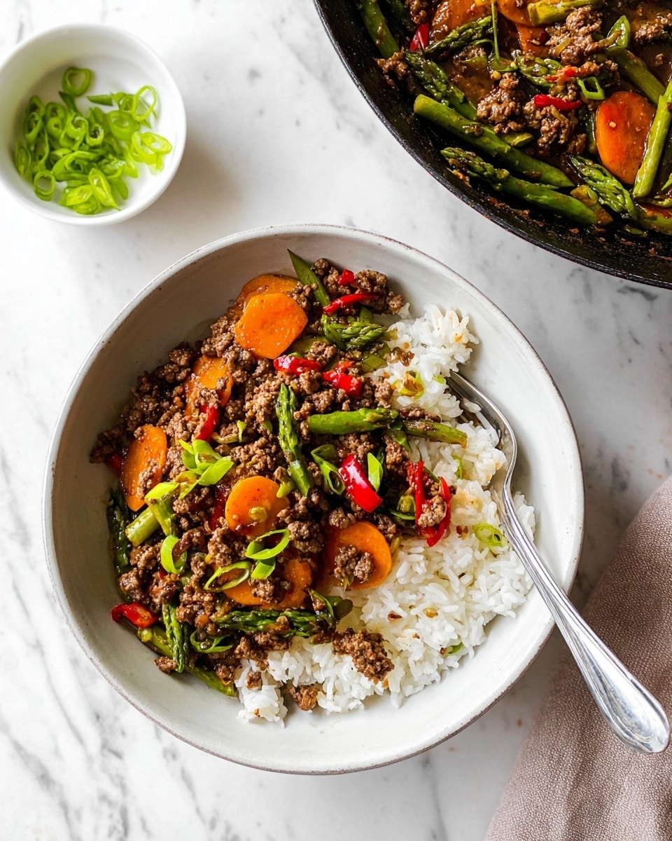The image shows a white bowl filled with steamed white rice on the right side and topped with three main layers on the left: a mixed stir fry of finely minced cooked beef with bright orange sliced carrots, green asparagus spears, small pieces of red bell pepper, and chopped green onions scattered on top. The textures include soft rice grains, tender cooked vegetables, and slightly crumbly ground beef. To the upper right corner, there is a black cooking pan with more of the same stir fry showing similar colors and textures. At the top left, a small white bowl contains chopped green onions. A silver fork rests inside the white bowl on the right side. The background is a white marbled surface. photo taken with an iphone --ar 4:5 --v 7