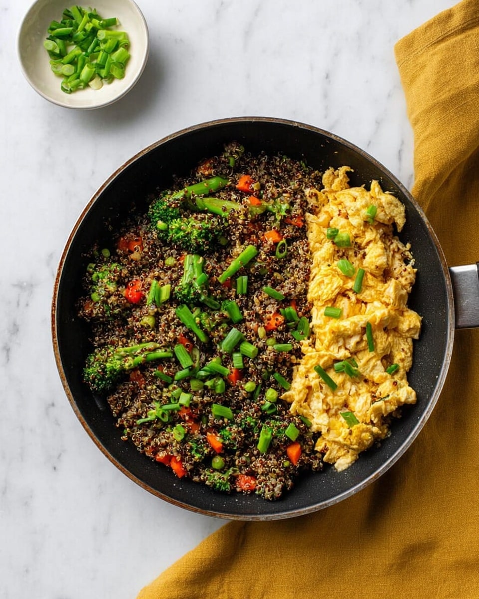 A black pan filled with a mixed dish where the bottom layer consists of a mix of quinoa and tiny bits of vegetables like broccoli, carrots, and red peppers, creating a speckled texture of green, orange, red, and black. On top of the right side of this mix is a layer of light golden scrambled eggs with a soft, fluffy texture. The dish is garnished with bright green chopped spring onions scattered over the quinoa and vegetables. The pan is placed on a white marbled surface with a mustard yellow cloth near the top right and a small white bowl with some green onion pieces at the top left. Photo taken with an iphone --ar 4:5 --v 7