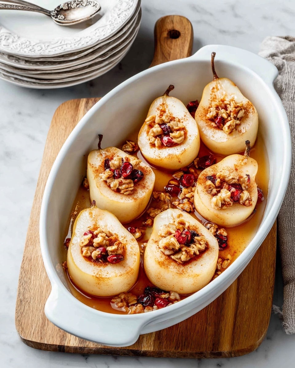 A white large oval baking dish holds eight halved pears, each with a hollow center filled with granola and small dried red berries. The pears are light creamy white with light brown edges and cinnamon sprinkled on top. A glossy syrup pools slightly at the bottom of the dish. The dish sits on a wooden cutting board over a white marbled surface. In the left background, there are stacked white plates and a decorative white plate with a silver spoon on it. Photo taken with an iphone --ar 4:5 --v 7