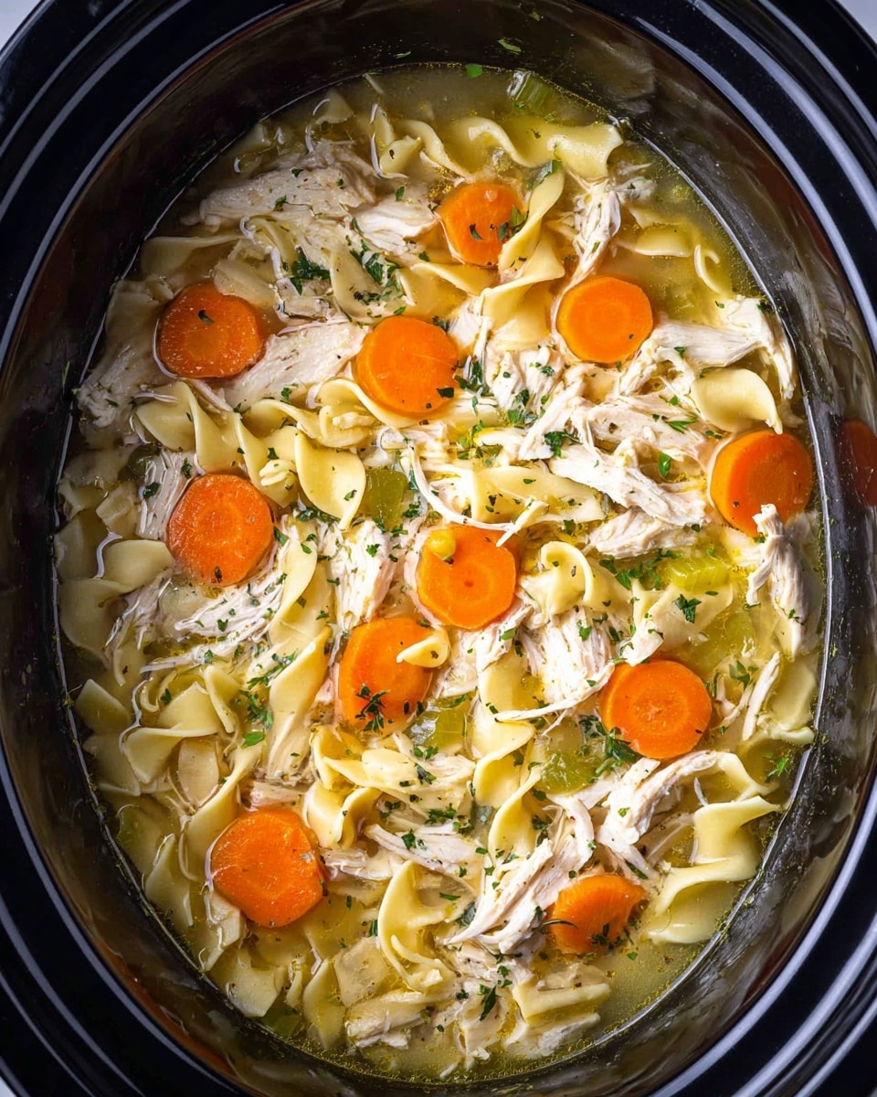 The image shows a close-up of chicken noodle soup inside a black slow cooker, resting on a white marbled surface. The soup has layers starting with a clear light golden broth at the bottom. On top lie wide, curly egg noodles in a cream-yellow color, mixed with shredded white chicken pieces spread evenly. Bright orange carrot slices and small chunks of pale green celery add color to the dish, with small green parsley flakes sprinkled on top. The soup also has visible pepper specks scattered throughout. The slow cooker’s round shape frames the soup nicely. photo taken with an iphone --ar 4:5 --v 7