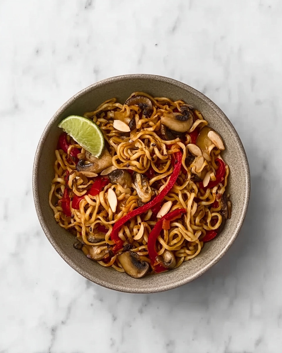 The image shows a gray bowl filled with noodles mixed with sliced mushrooms, red bell pepper strips, and pieces of almond. On top, there is a small lime wedge placed slightly to the side. The bowl sits on a white marbled surface. The noodles are light brown with a slight shine, the mushrooms have a beige color with darker edges, and the red peppers add bright color contrast. Photo taken with an iphone --ar 4:5 --v 7