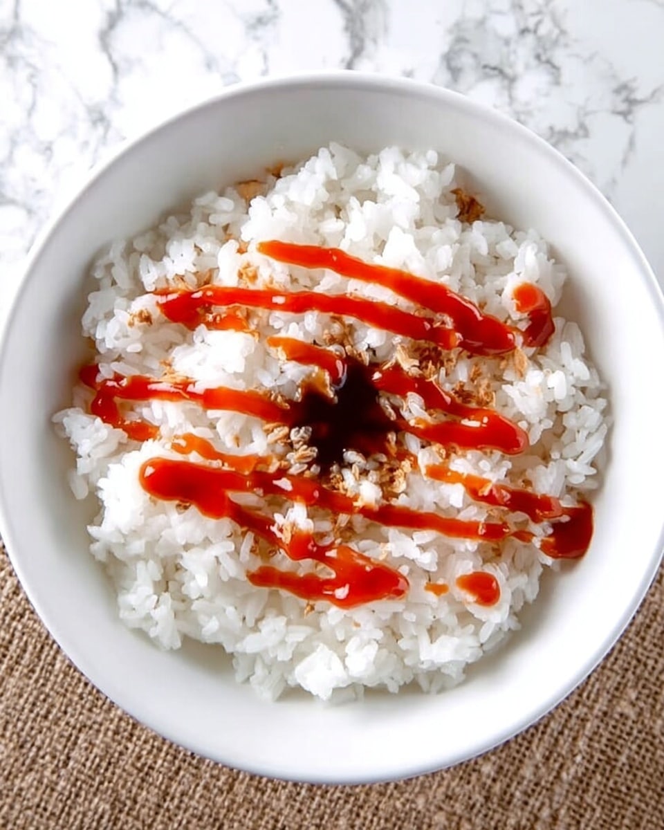 A white bowl filled with plain white rice topped with a thin drizzle of dark brown soy sauce in the center and bright red sriracha sauce zigzagged evenly over the rice. The bowl is placed on a white marbled surface. Photo taken with an iphone --ar 4:5 --v 7