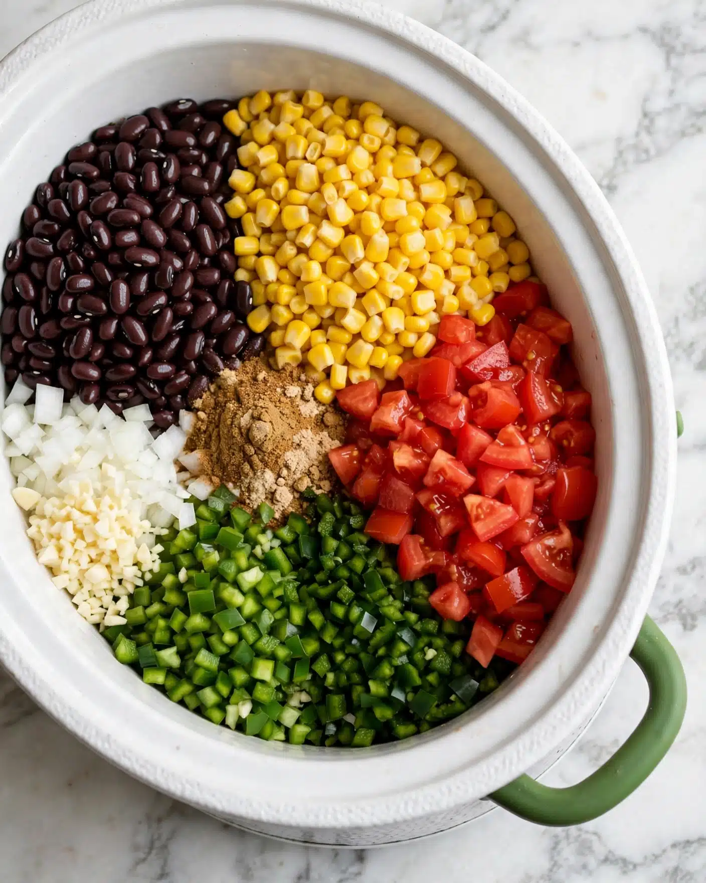 Inside a white slow cooker with a green handle, there are seven main layers arranged side by side without mixing. The top left section shows dark brown black beans with a shiny, smooth texture. Next to it on the right is a large pile of bright yellow corn kernels, looking soft and plump. Below the corn, red diced tomatoes cover the right edge with a juicy texture. Below the tomatoes is a layer of finely chopped dark green jalapeño peppers, and next to them on the left are more green chopped bell peppers with a slightly lighter color. Toward the bottom left edge, there are small, white chopped onion pieces and finely chopped garlic cloves. In the center, there is a pile of mixed brown spices with a powdery texture. All this sits on a white marbled surface beneath the cooker. Photo taken with an iphone --ar 4:5 --v 7