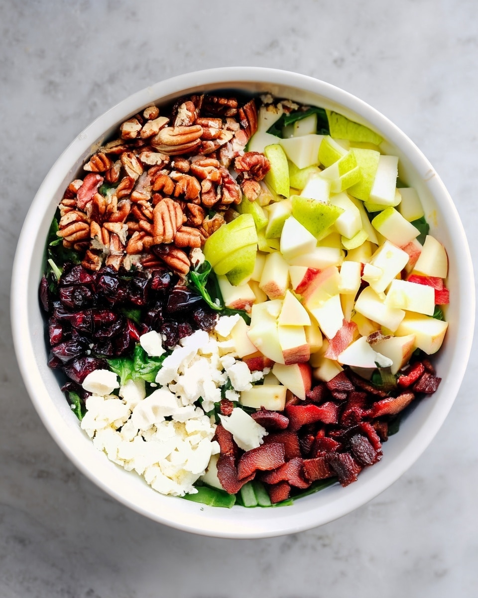 A white bowl sits on a white marbled surface filled with a fresh salad made up of six distinct sections. Starting from the top left, there is a pile of light brown pecans with a rough texture. Moving clockwise, there are light green and white small pieces of diced pear. Next to the pear, there are light yellow and red small apple pieces. Below the apples, there are dark reddish-brown cooked bacon bits. To the left of the bacon, there is a white fluffy layer of crumbly cheese, likely feta or goat cheese. Finally, below the pecans, there is a small pile of dark red dried cranberries. The base of the salad is visible underneath, made up of dark green leafy vegetables. photo taken with an iphone --ar 4:5 --v 7